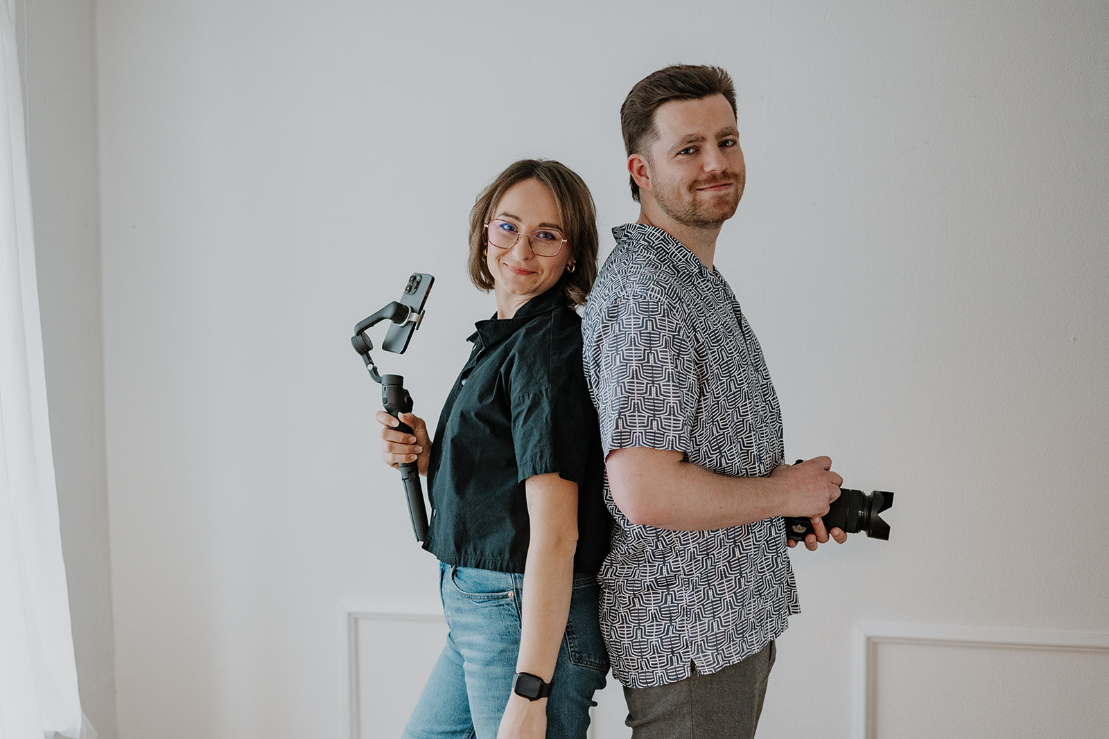 Die beiden Geschäftsführer stehen Rücken an Rücken mit Technik ein der Hand und sehen in die Kamera.