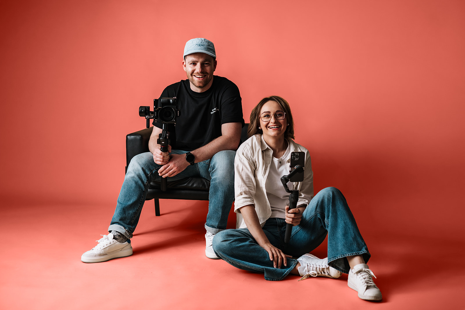 Geschäftsführer sitzen auf dem Boden bzw. auf dem Stuhl und sehen sich an mit Equipment, der Hintergrund ist farbig, die Personen sind schwarz-weiß