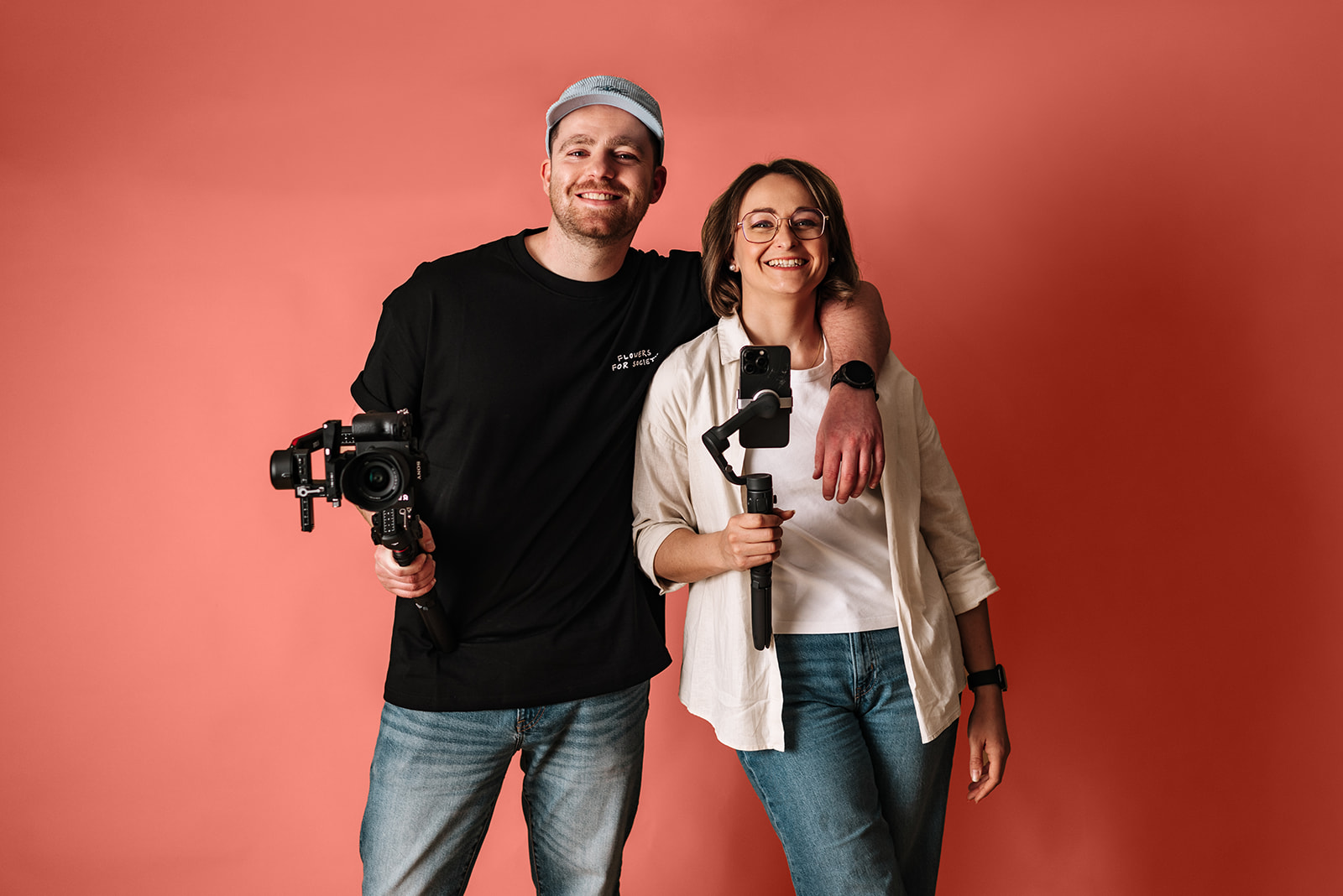 Geschäftsführer stehen vor einer farbigen Wand mit Equipment und lachen in die Kamera